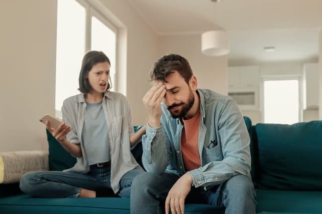 Angry couple or marriage fighting for a mobile phone at home. Jealous caucasian woman holding smart phone and showing message to his husband. Angry girlfriend asking for an explanation to her cheater boyfriend, point at his smartphone
