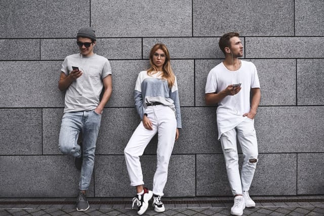 Fashion portrait of Three best friends posing at street, wearing stylish outfit and jeans against gray wall .