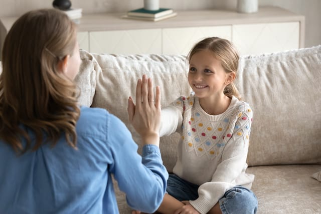 Happy adorable small child girl giving high five to loving young mother, finishing practicing correct sounds pronunciation. Professional female speech therapist praising little patient for success.