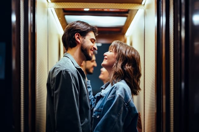 Smiling boyfriend looking at his girlfriend while laughing and standing together in the elevator.