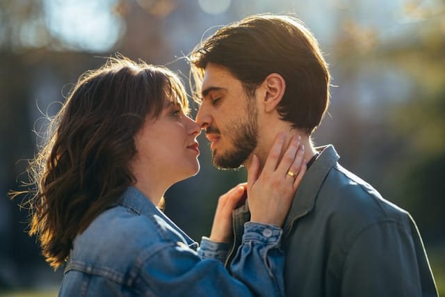 Close up photo of girlfriend embracing and kissing her boyfriend while standing together at the city street.