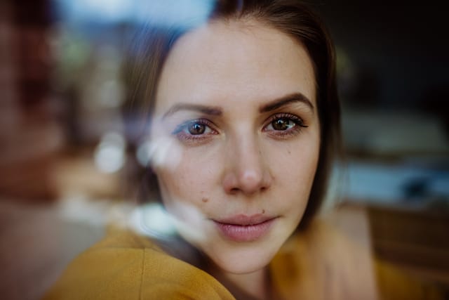 Close-up portrait of happy young woman resting and daydreaming at home, shot through window.