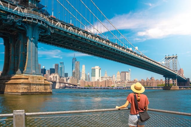 Young woman enjoying view of city skyline in New York. Happy lifestyle girl with hat traveling tourist on bridges. High quality photo