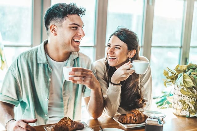 Happy couple enjoying breakfast drinking coffee at bar cafeteria - Life style concept with guy and girl in love having date moment sitting at restaurant in the city centre