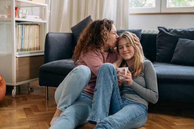 mother kiss her daughter while sitting on floor in living room