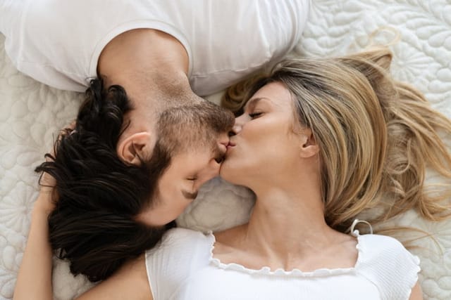 Top view of loving caucasian couple kissing and cuddling, lying in bed. Spouses expressing affection, love and enjoying sensual pleasure. Love and relationships concept