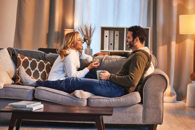 Couple relax in living room, conversation with coffee and spending quality time together at home at the weekend. Love, care and trust, people having a chat with communication, hot drink and happiness