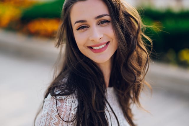 Portrait of a happy fashionable young brunette smiling at the camera outdoors.
