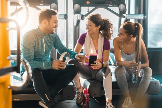 Small group of athletic people communicating during water break in a gym. Funny man telling jokes to the girls during the gym workout.