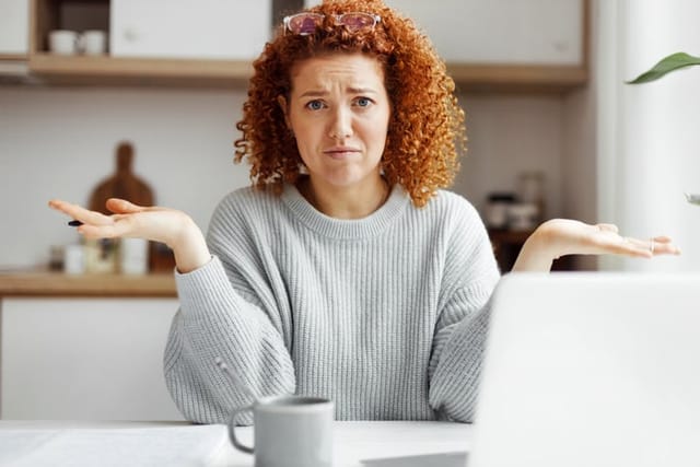Confused puzzled and upset female accountant working from home at kitchen table, having troubles with laptop internet connection or annual financial report, looking at camera frowning and shrugging