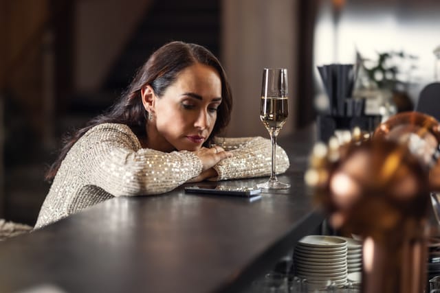A nervous woman is impatiently looking at her mobile phone because she is waiting for a man with whom she arranged a date and he is late or did not come.