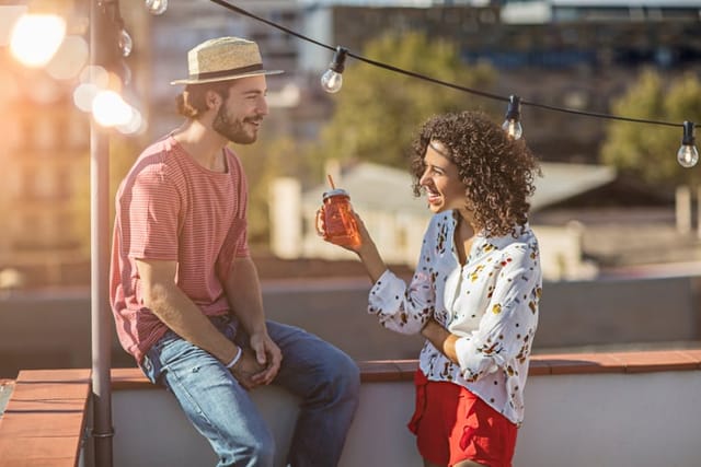 Outdoor shot of young couple with drinks talking on a rooftop party
