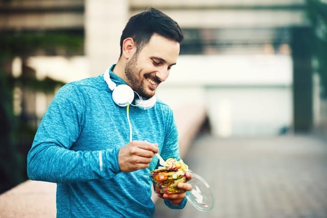 man eating salad with headphones outdoors