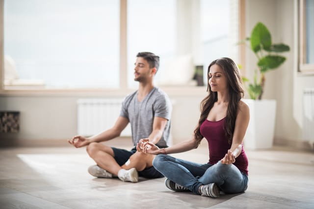Young couple meditating in Lotus position in their new apartment.