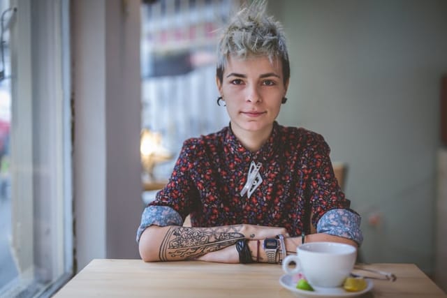 Young and lovely gender blend woman, enjoying a cup of coffee at the cafe.