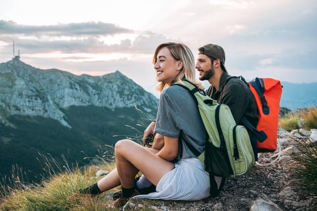 happy man, woman sitting on mountaintop hiking