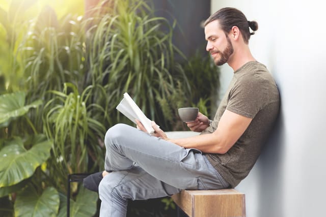 man reading book outside on bench