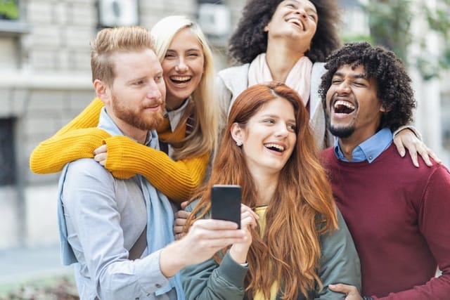 Multi-ethnic group of friends laughing at funny message outdoor