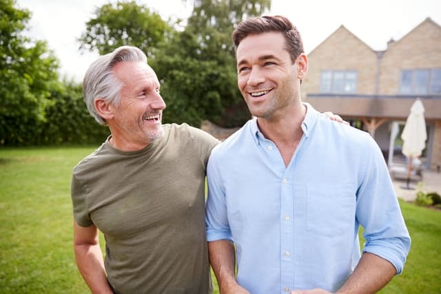 Senior Father And Adult Son Walking And Talking In Garden Together