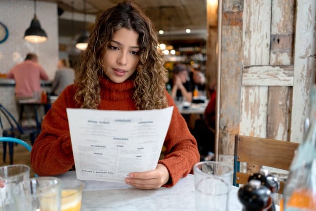 Portrait of a woman at a restaurant reading the menu - food and drink concepts
