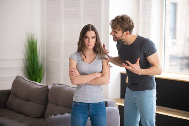 Conflict. Young long-haired woman standing with her arms clasped while her husband shouting