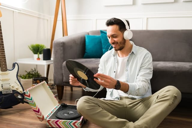 Cheerful young man putting a vinyl record on a turntable and listening to music with headphones at home