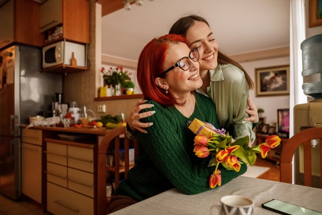 Copy space shot of happy mature woman embracing her caring daughter who is surprising her with a gift and a beautiful bouquet of tulips for Mother's day.