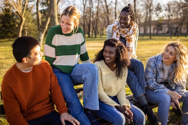 Group od cheerful multiracial female and male friends, sitting on the park bench and talking