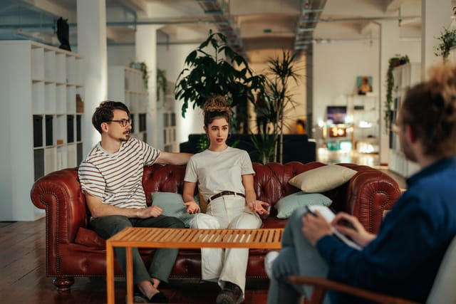 Young adult couple at psychologist therapy. They are sitting on sofa in doctor office, having a consultation with a doctor