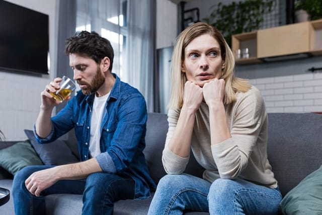 Young family falls apart, depressed woman because of alcoholic husband, couple sitting on sofa in living room