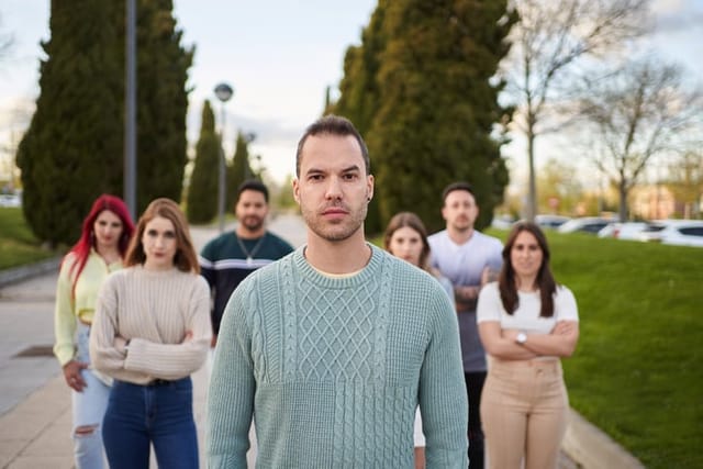 Man looking serious at the camera while standing in front of a group of people. Team and leadership concept.