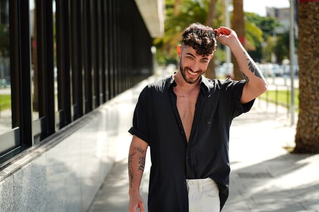 Photo of happy young man in casual shirt looking at camera. Smiling man with beard on the city street. Tourist.