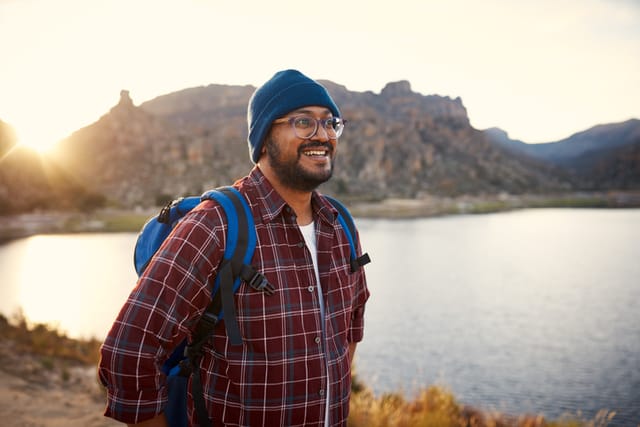 smiling man in glasses, beanie going for a hike at sunset