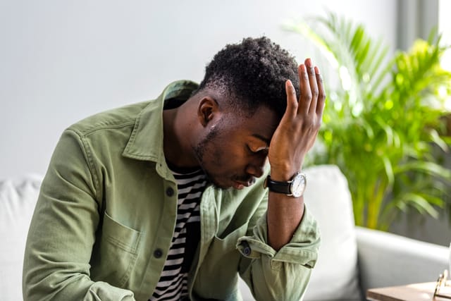 man on couch covering head with palm