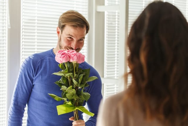 Selective focus shot of romantic mid adult man smiling and smelling the roses he is about to give to his loving wife.
