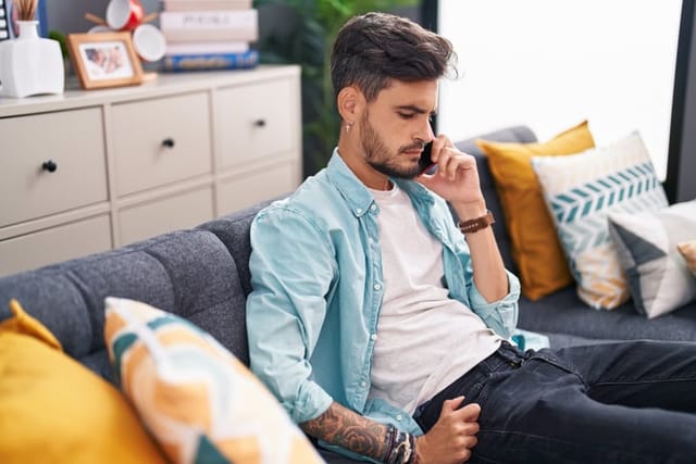 Young hispanic man talking on smartphone with worried expression at home
