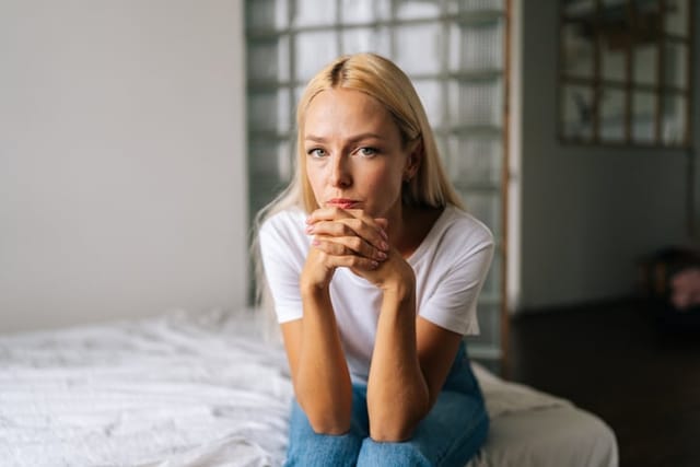 serious blonde woman sitting on bed