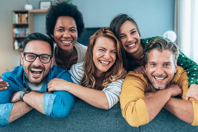 Portrait of group of friends sitting on the sofa at home smiling and looking at camera. Young people looking happy together, embracing together, wearing colorful, modern casual clothing. Multi ethnic group of young people