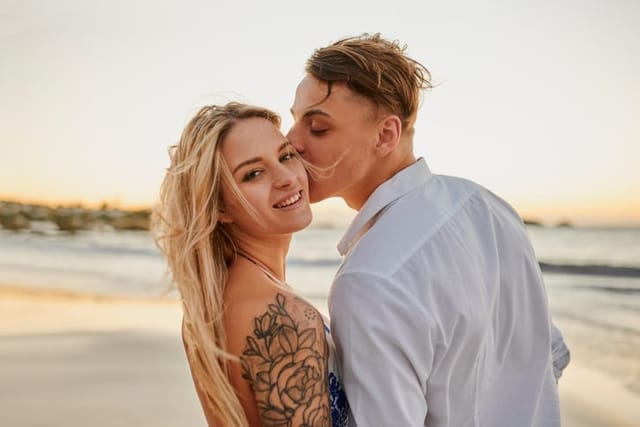 happy couple kissing on cheek on beach