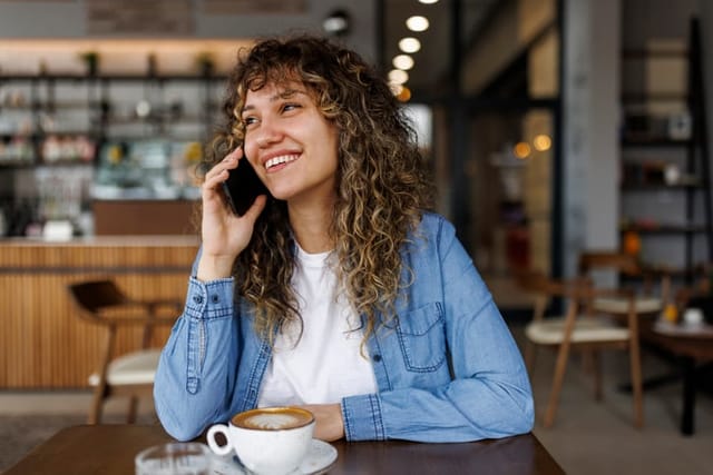 Happy young woman talking on mobile phone and enjoying coffee drink in a coffee shop