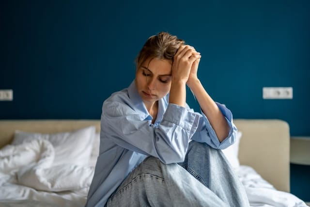Young unhappy woman sitting on bed at home, waking up depressed, suffering from depression, feeling sad and miserable. Female suffering from post-traumatic stress disorder. Women and mental health