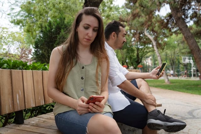 couple busy with smartphones, talking to virtual friends and ignoring each other at park