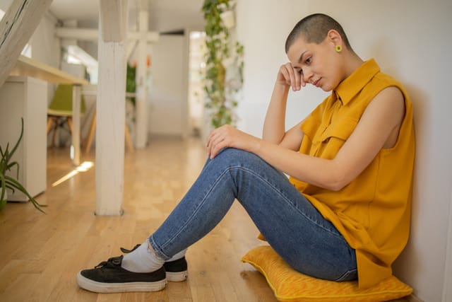young woman yellow shirt sitting against wall