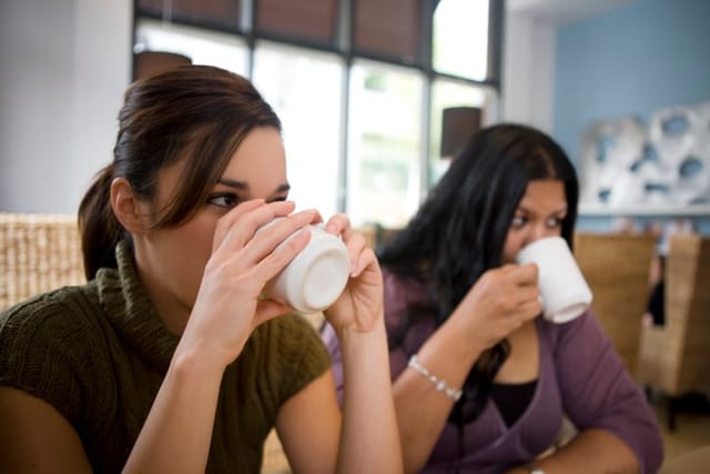 two female friends drinking from coffee mugs