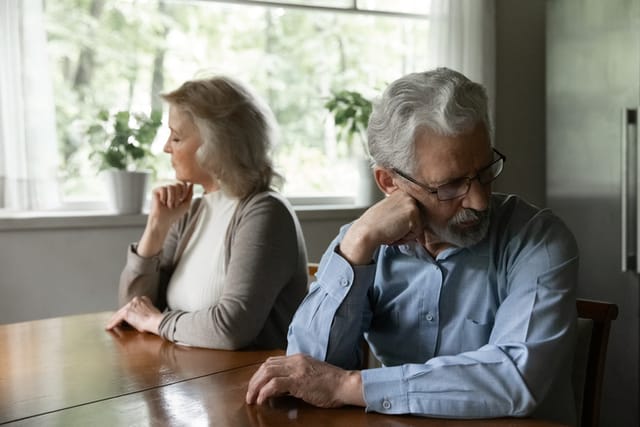 Upset senior husband wife sit at table separately avoid talking