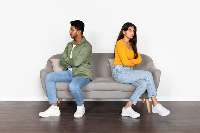 Indian couple, visibly upset, engage in silent quarrel, sitting together yet emotionally apart, embodying offense and ignoring each other, reflecting a rift