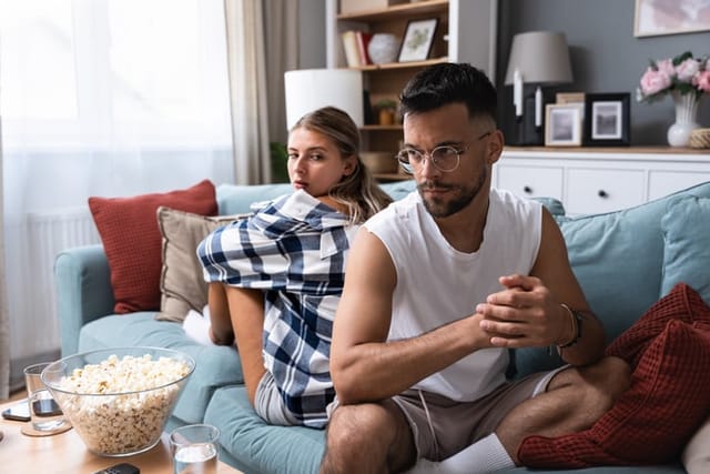Stressed young married couple sitting separately on different sides of sofa ignoring each other after quarrel. Offended spouses not talk communicate feeling depressed disappointed after argue.