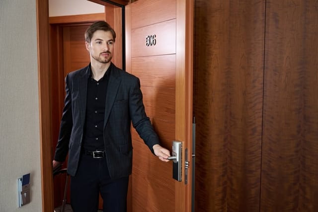 Young thoughtful businessman in suit opening a door and looking around hotel room
