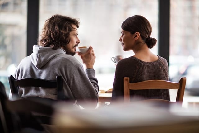Rear view of young couple talking to each other while sitting in a cafe and drinking coffee.