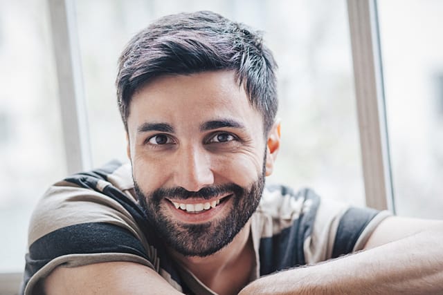 Portrait of young middle eastern Turkish man smiling, posing and sitting in cafeteria